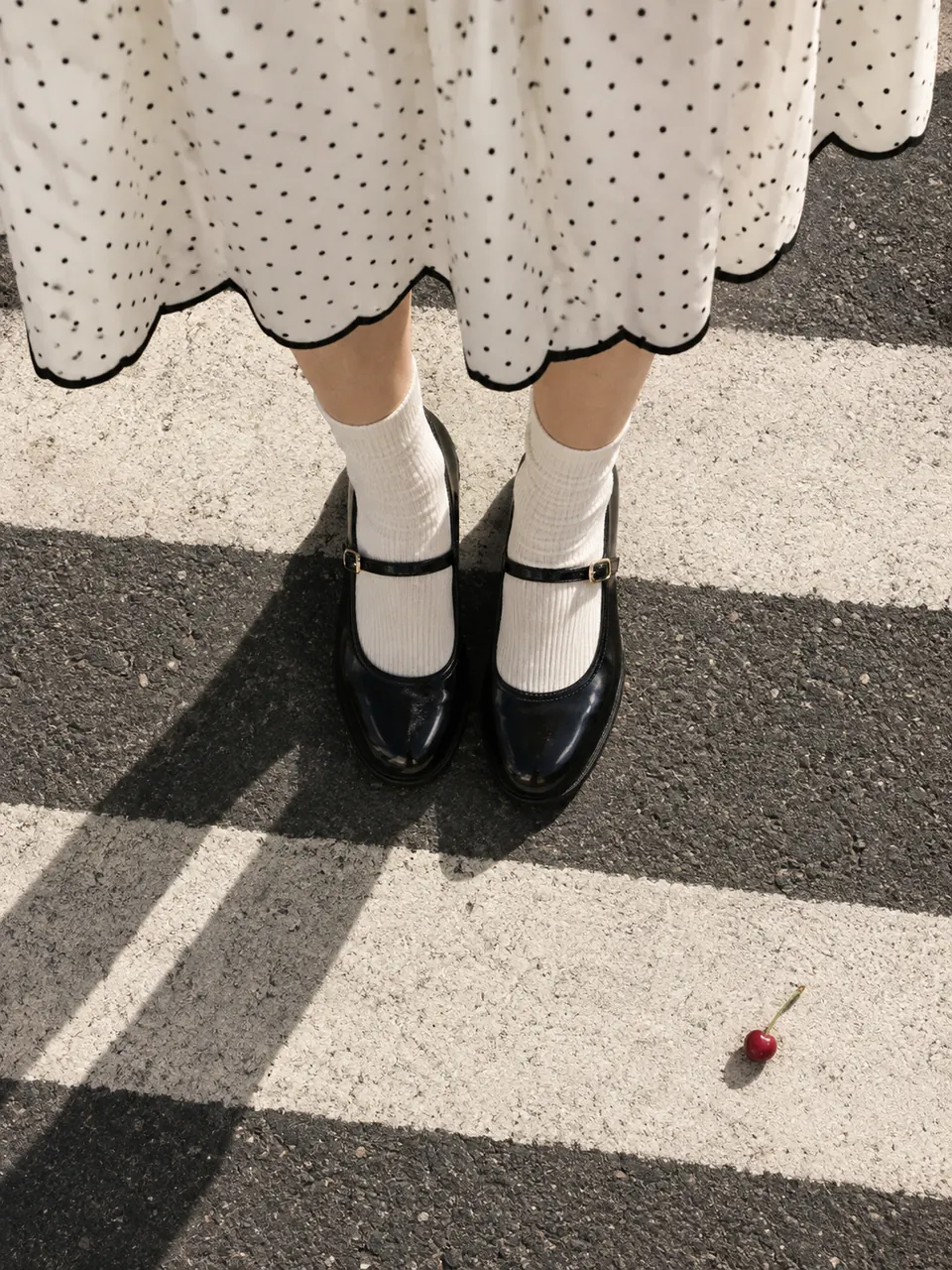 Blick hinunter auf einen Zebrastreifen: Mary-Jane-Schuhe und der Saum mit Bogenkante eines Pin Dot-Rocks.