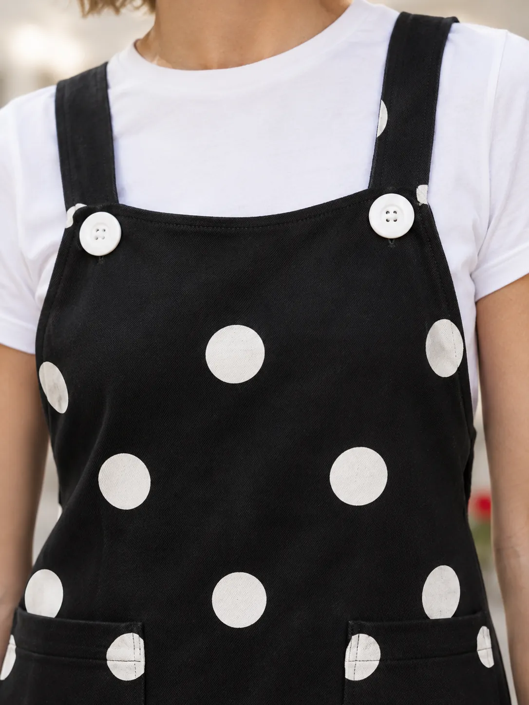 Bakery Queue Pinafore, close-up: the curved bib with two large round white buttons and the coin dots